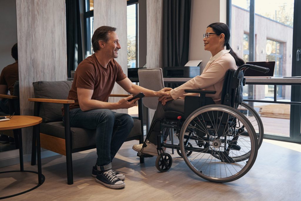 Das Bild zeigt einen Mann der die Hand einer Frau im Rollstuhl hält.